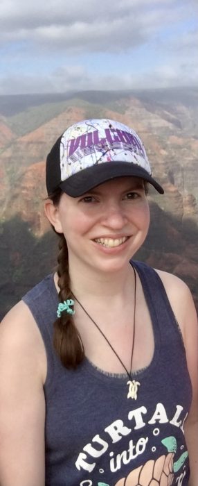 A brown-haired girl in a hat smiling at the camera with Waimea Canyon in the background